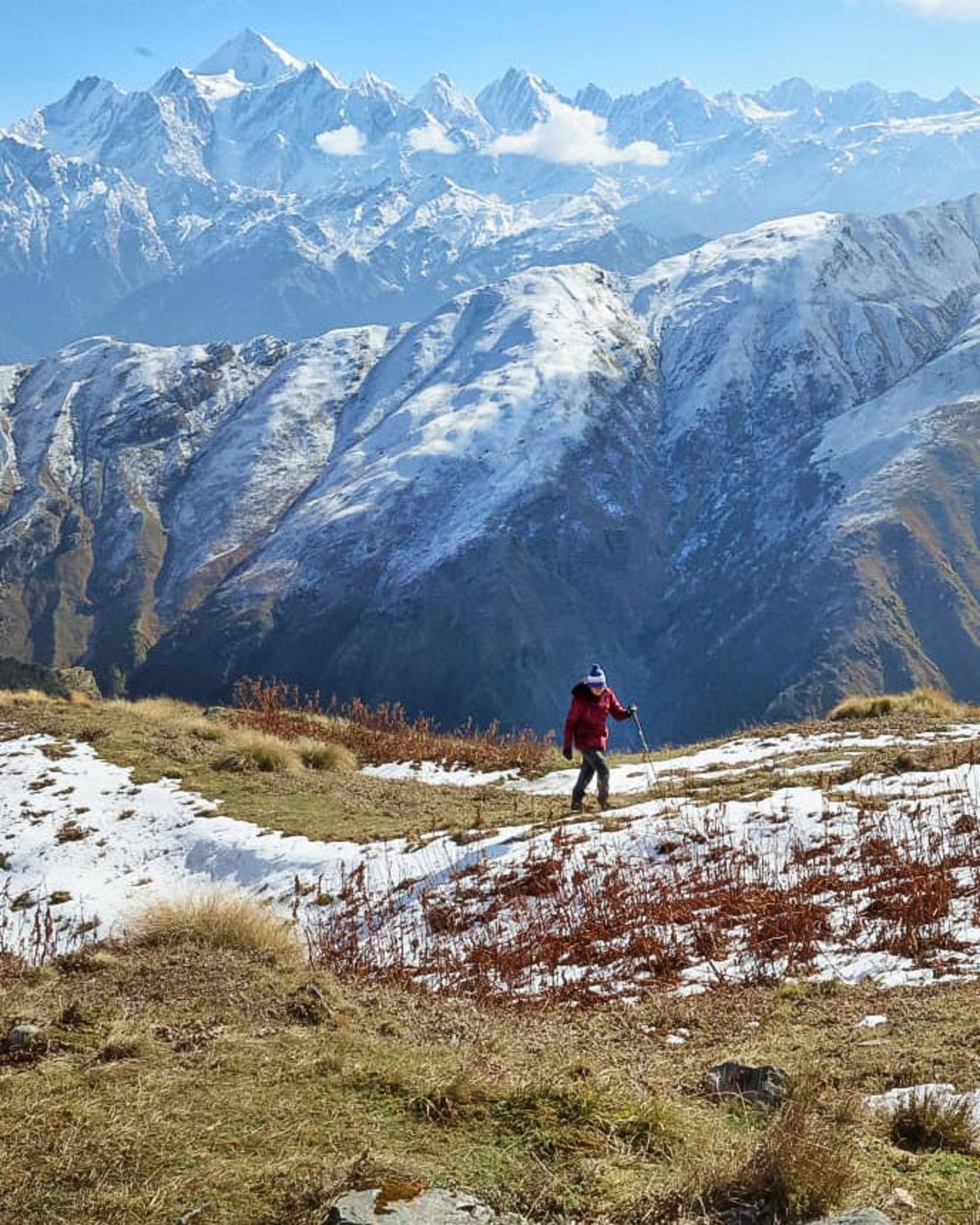 A trekker walking with snow capped-mountains in the background at the Ranthan Kharak trek